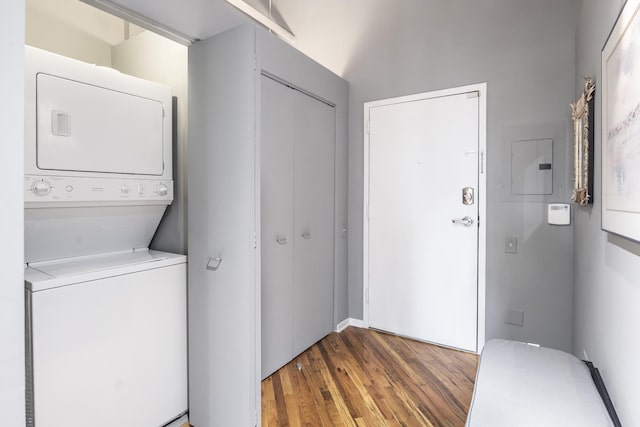 washroom with stacked washer / drying machine, laundry area, electric panel, and wood finished floors