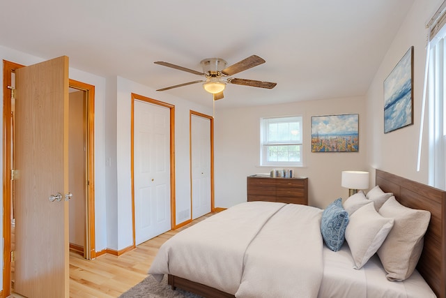 bedroom featuring ceiling fan, multiple closets, and light wood-type flooring