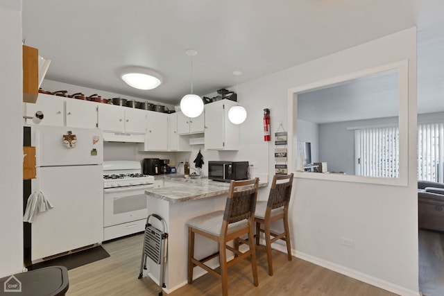 kitchen with white appliances, hanging light fixtures, a kitchen breakfast bar, white cabinets, and kitchen peninsula