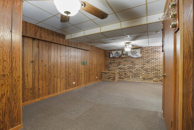 basement featuring brick wall, carpet, a paneled ceiling, and wooden walls