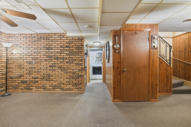 hallway with carpet flooring, brick wall, a drop ceiling, washer / clothes dryer, and wood walls