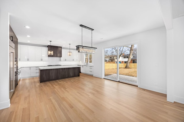 kitchen featuring a kitchen island, white cabinets, hanging light fixtures, dark brown cabinetry, and light wood-type flooring