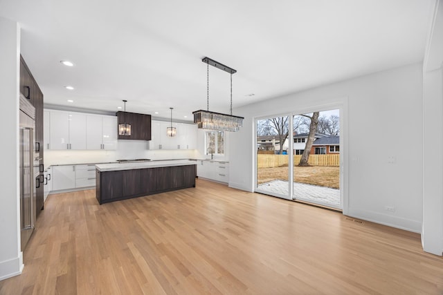 kitchen with light hardwood / wood-style flooring, white cabinetry, dark brown cabinets, a kitchen island, and decorative light fixtures