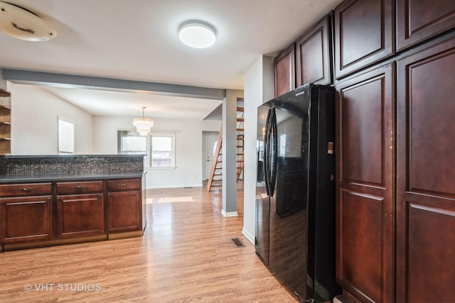 kitchen with light wood-type flooring, an inviting chandelier, black fridge with ice dispenser, and decorative light fixtures