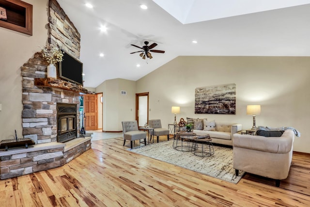 living room with high vaulted ceiling, a stone fireplace, wood finished floors, and a ceiling fan