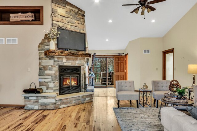 living room with ceiling fan, a stone fireplace, wood-type flooring, and visible vents