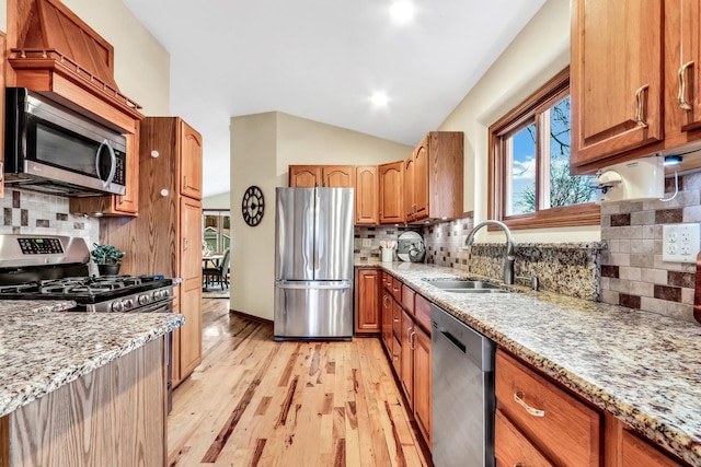 kitchen featuring lofted ceiling, appliances with stainless steel finishes, a sink, light stone countertops, and light wood-type flooring