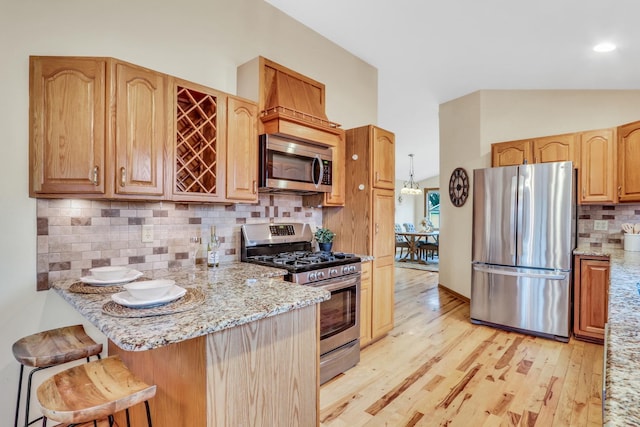 kitchen with stainless steel appliances, light wood-style floors, backsplash, light stone countertops, and a kitchen bar