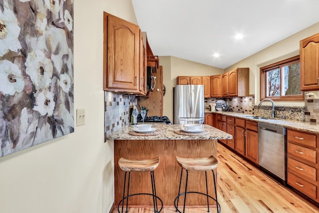 kitchen featuring lofted ceiling, a breakfast bar area, appliances with stainless steel finishes, a peninsula, and a sink