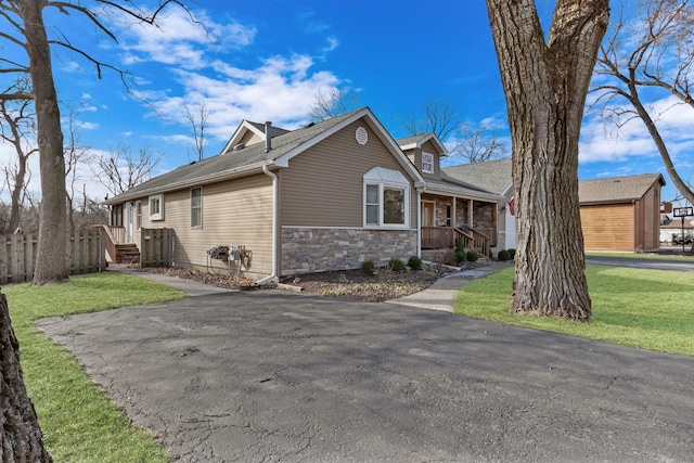 view of front of house with stone siding, covered porch, and a front yard