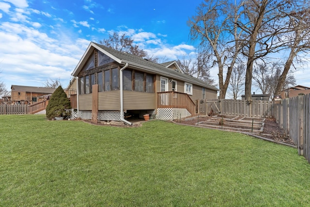 rear view of house featuring a sunroom, a lawn, a fenced backyard, and a garden