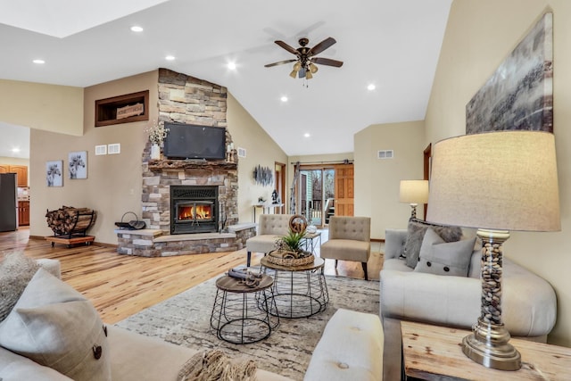 living room featuring visible vents, ceiling fan, wood finished floors, a stone fireplace, and high vaulted ceiling