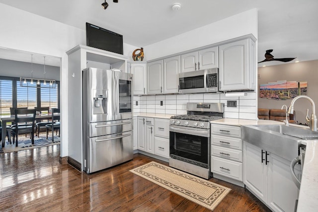 kitchen featuring dark wood-type flooring, sink, appliances with stainless steel finishes, ceiling fan, and backsplash