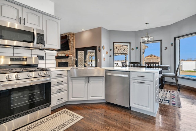 kitchen with appliances with stainless steel finishes, dark hardwood / wood-style floors, sink, hanging light fixtures, and kitchen peninsula