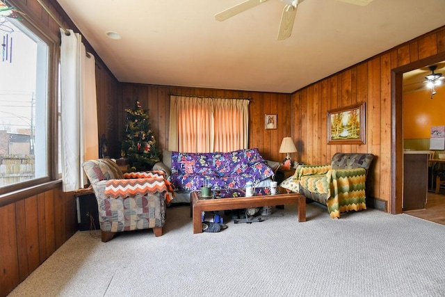 carpeted living room with ceiling fan and wood walls