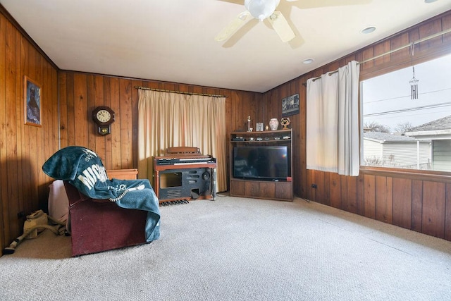 sitting room with light colored carpet, ceiling fan, and wood walls