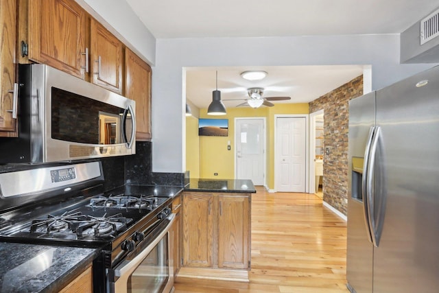 kitchen with ceiling fan, dark stone countertops, stainless steel appliances, light hardwood / wood-style floors, and kitchen peninsula