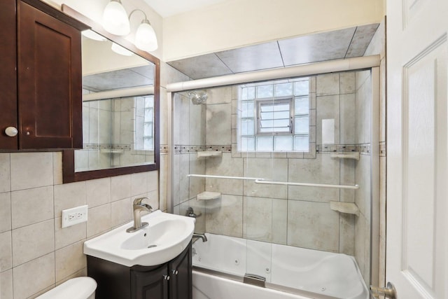 full bathroom featuring vanity, bath / shower combo with glass door, toilet, and tile walls