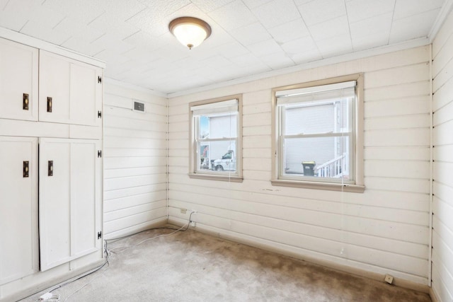 unfurnished room featuring ornamental molding, light colored carpet, and wood walls