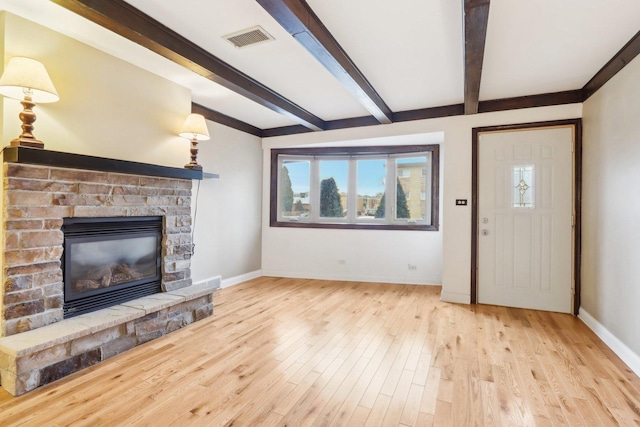 living room with beamed ceiling, a stone fireplace, and light hardwood / wood-style flooring