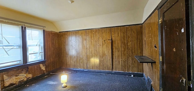 empty room featuring vaulted ceiling and wooden walls