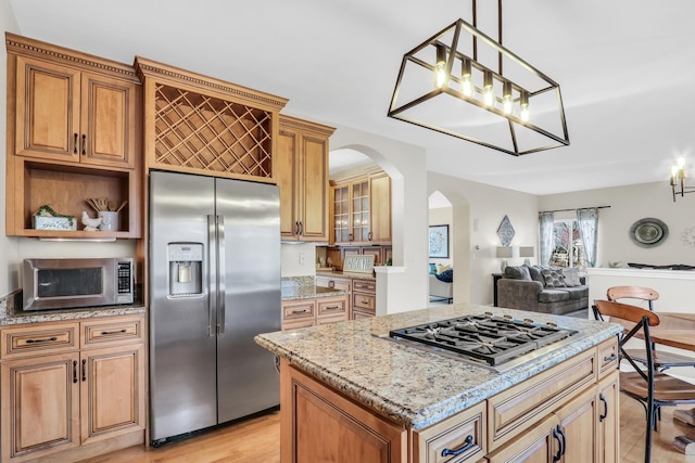 kitchen featuring light stone counters, decorative light fixtures, light hardwood / wood-style flooring, a kitchen island, and stainless steel appliances