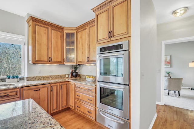 kitchen with stainless steel double oven, light stone counters, and light hardwood / wood-style flooring