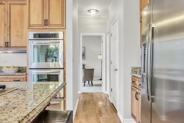 kitchen featuring light wood-type flooring, light stone countertops, and appliances with stainless steel finishes