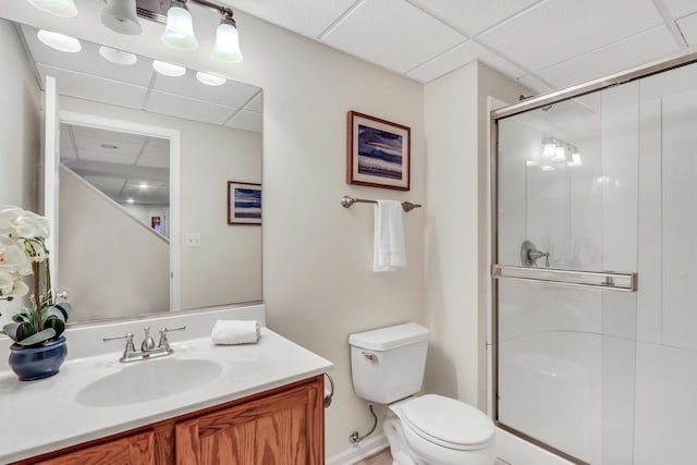 bathroom with vanity, toilet, a drop ceiling, and a shower with shower door