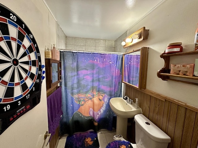 bathroom with tile patterned floors, toilet, sink, and wood walls