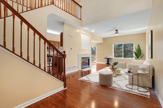 living room featuring a tiled fireplace, hardwood / wood-style flooring, ceiling fan, and a high ceiling