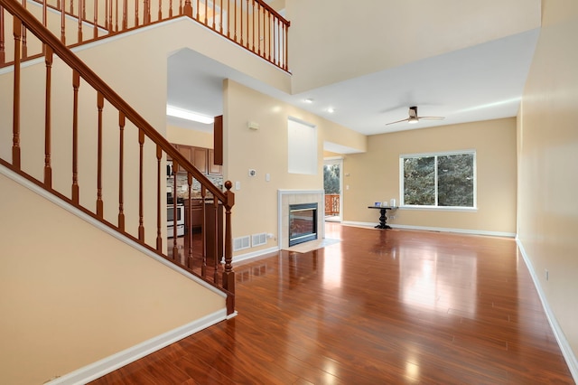 unfurnished living room with hardwood / wood-style floors, a tile fireplace, ceiling fan, and a high ceiling