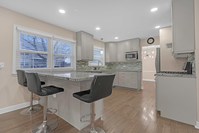 kitchen featuring gray cabinetry, stainless steel microwave, tasteful backsplash, a kitchen bar, and light wood-type flooring