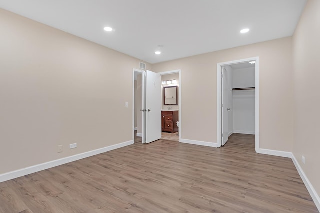 unfurnished bedroom featuring connected bathroom, a walk in closet, light hardwood / wood-style flooring, and a closet