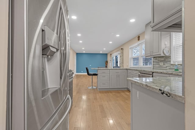 kitchen with appliances with stainless steel finishes, a kitchen breakfast bar, decorative backsplash, light hardwood / wood-style floors, and kitchen peninsula