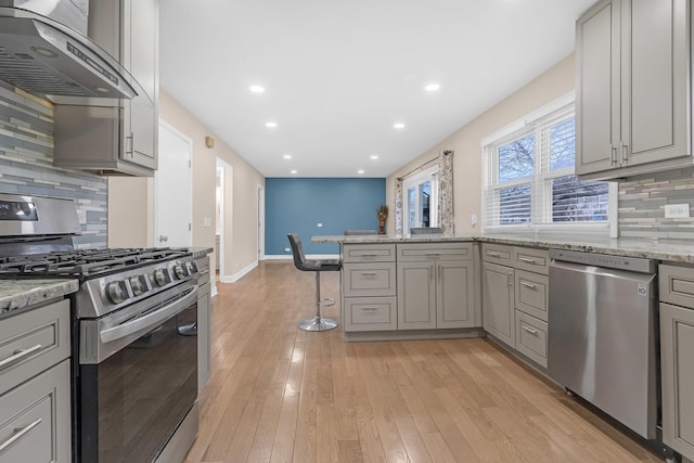 kitchen featuring stainless steel appliances, gray cabinetry, exhaust hood, and light stone counters