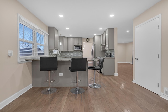 kitchen with gray cabinetry, tasteful backsplash, a breakfast bar, and appliances with stainless steel finishes