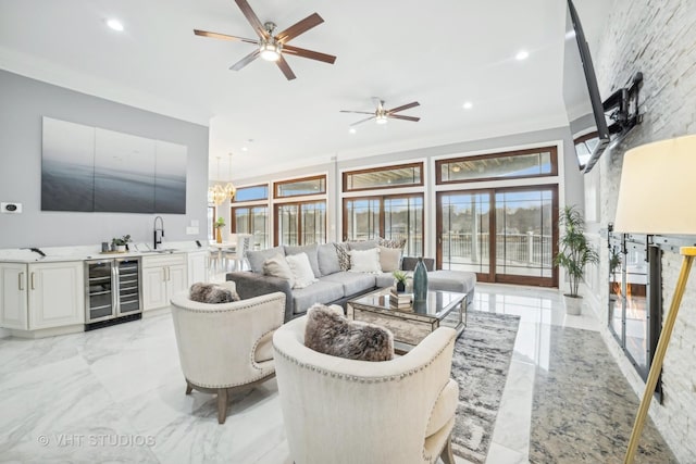 living room with wine cooler, sink, crown molding, and ceiling fan with notable chandelier