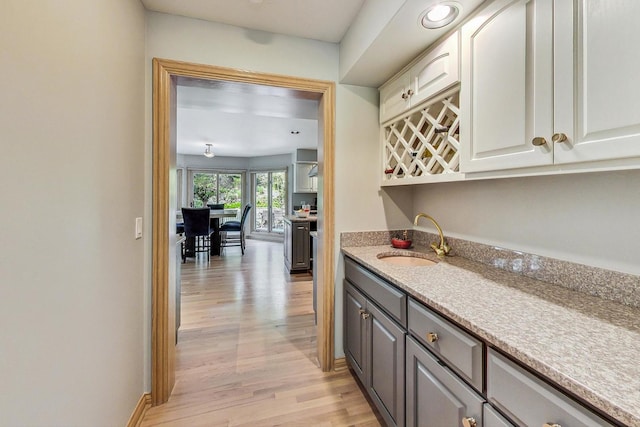 bar with light stone counters, light hardwood / wood-style floors, sink, and gray cabinetry