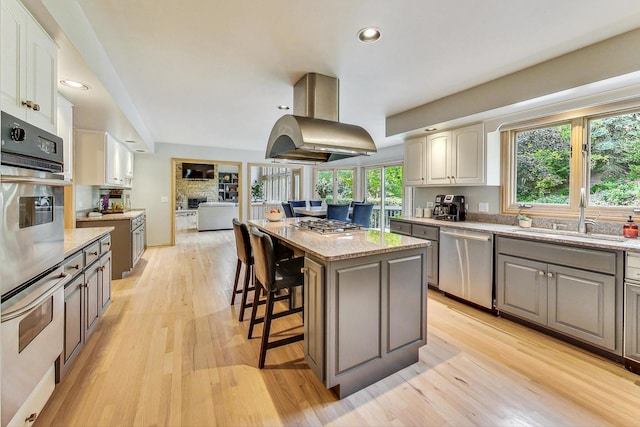 kitchen featuring a kitchen island, appliances with stainless steel finishes, sink, a kitchen bar, and island exhaust hood