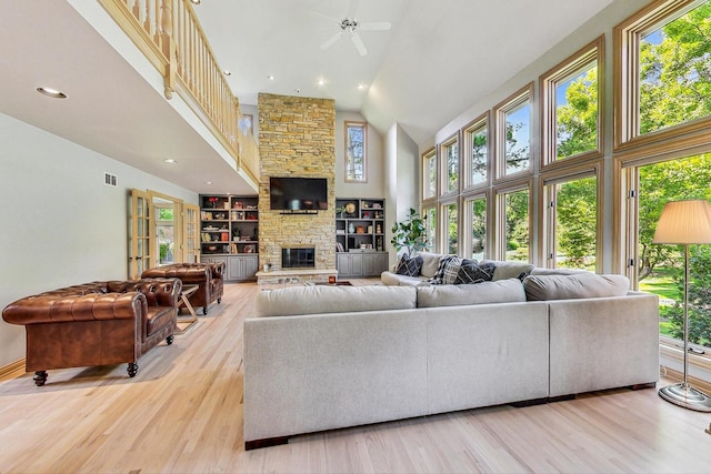 living room featuring high vaulted ceiling, a healthy amount of sunlight, a fireplace, and light hardwood / wood-style flooring