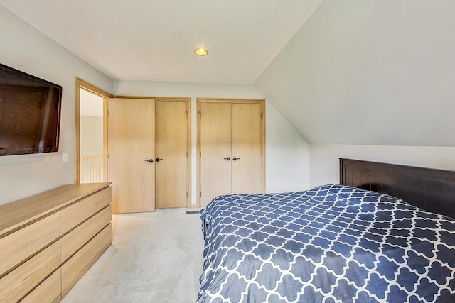 carpeted bedroom featuring two closets and vaulted ceiling