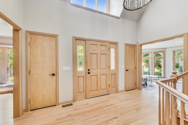 foyer entrance with high vaulted ceiling, a chandelier, and light wood-type flooring