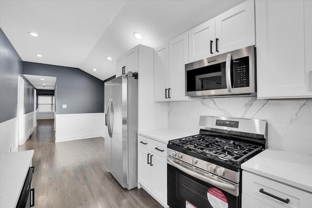 kitchen featuring white cabinetry, hardwood / wood-style floors, stainless steel appliances, light stone counters, and vaulted ceiling