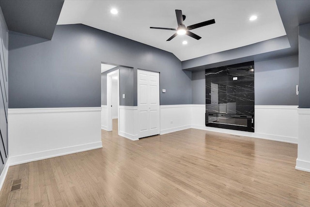 spare room featuring vaulted ceiling, light hardwood / wood-style floors, a premium fireplace, and ceiling fan