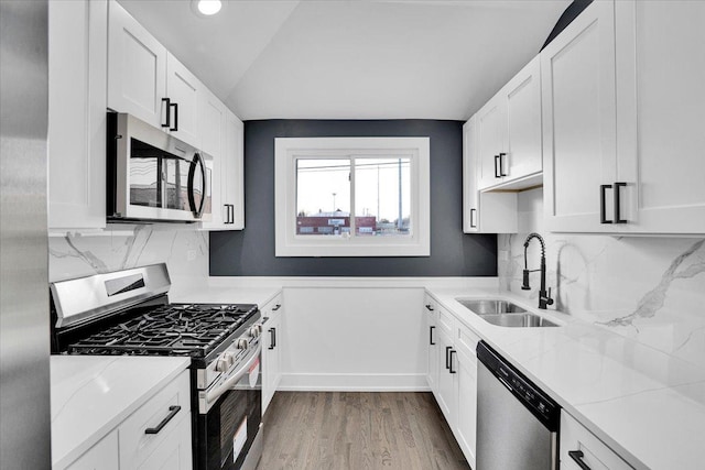 kitchen featuring lofted ceiling, sink, white cabinets, light stone counters, and stainless steel appliances