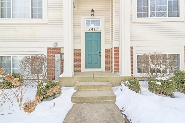 snow covered property entrance featuring brick siding