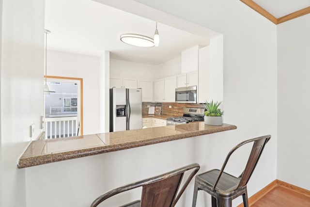 kitchen with stainless steel appliances, tasteful backsplash, hanging light fixtures, white cabinets, and a peninsula