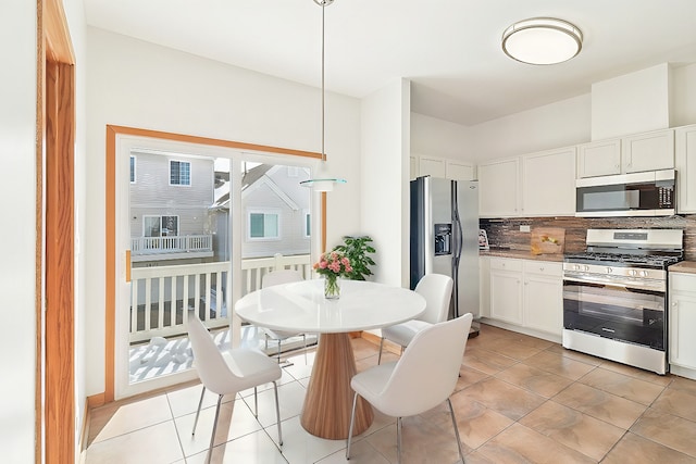 kitchen with light tile patterned floors, white cabinetry, appliances with stainless steel finishes, backsplash, and decorative light fixtures