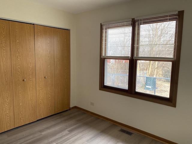 unfurnished bedroom featuring multiple windows, light hardwood / wood-style floors, and a closet